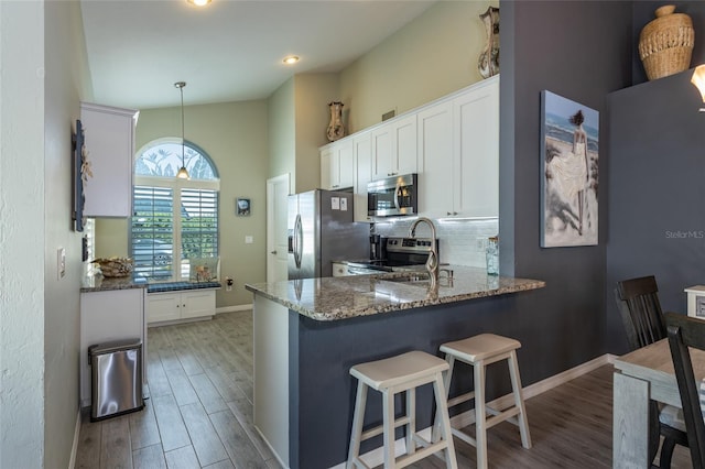 kitchen featuring white cabinetry, hanging light fixtures, dark stone counters, kitchen peninsula, and stainless steel appliances