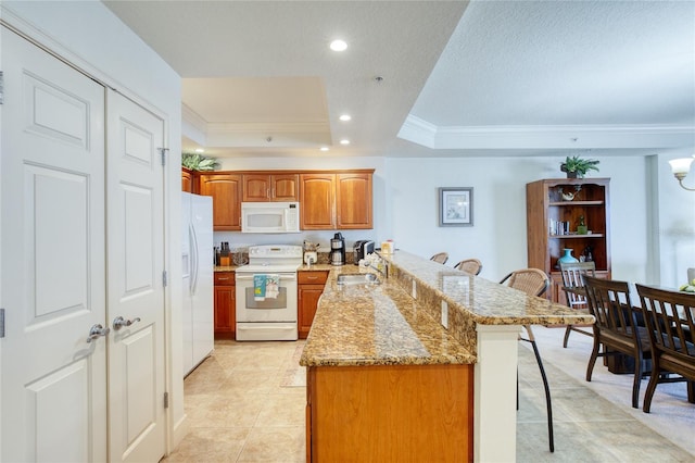 kitchen with a kitchen bar, sink, a raised ceiling, kitchen peninsula, and white appliances