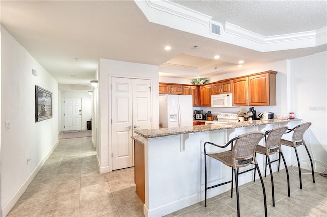 kitchen with white appliances, a tray ceiling, light stone countertops, a textured ceiling, and kitchen peninsula