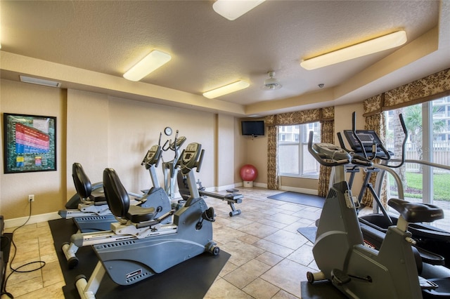 exercise room featuring a raised ceiling, plenty of natural light, and a textured ceiling