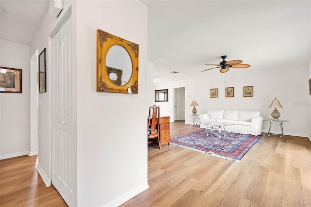 living area with light wood-style floors, baseboards, and a ceiling fan