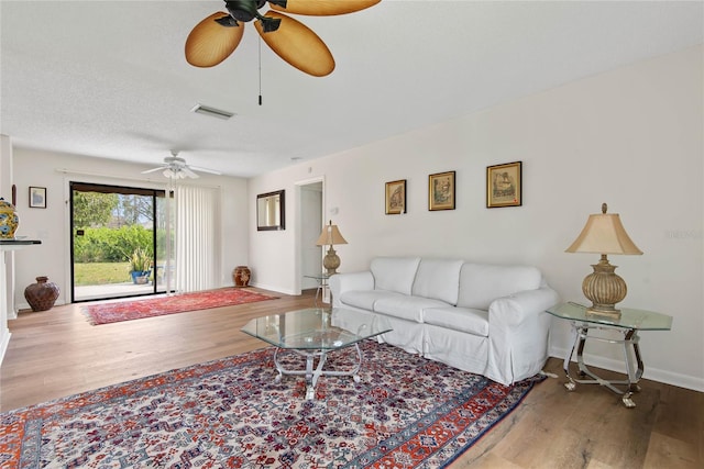 living room with ceiling fan, wood finished floors, visible vents, and baseboards