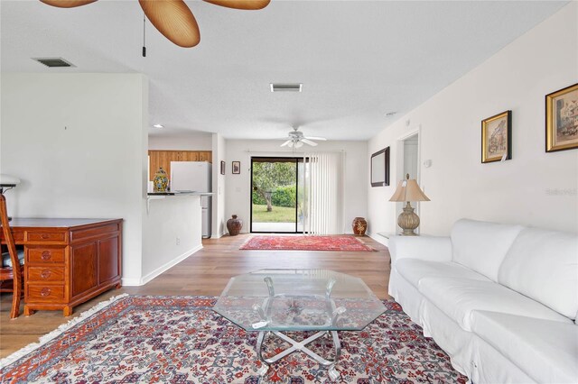 living room with a ceiling fan, visible vents, and wood finished floors