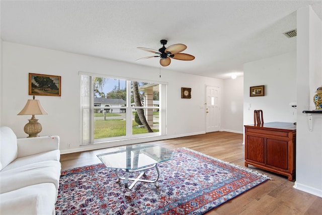 living room featuring a ceiling fan, baseboards, visible vents, and wood finished floors