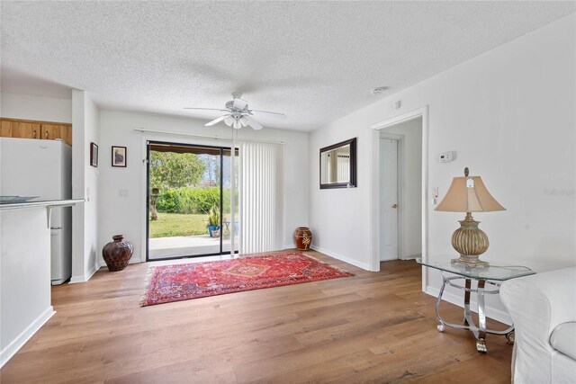 doorway to outside with baseboards, ceiling fan, light wood-style flooring, and a textured ceiling