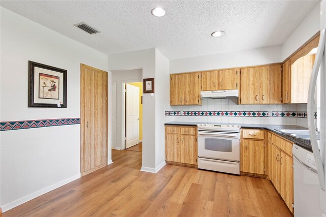 kitchen with white appliances, tasteful backsplash, light wood finished floors, visible vents, and under cabinet range hood