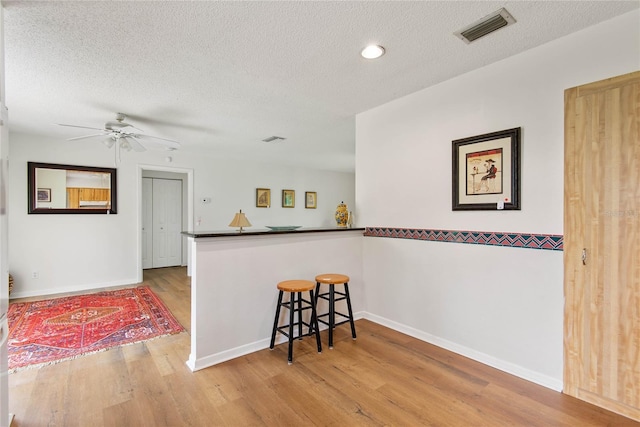 kitchen with dark countertops, visible vents, a textured ceiling, wood finished floors, and a kitchen bar