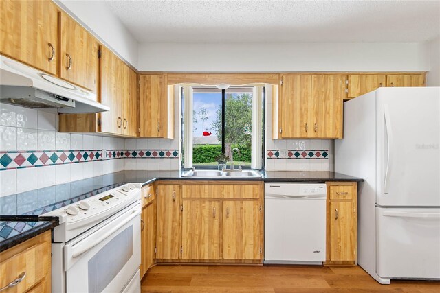 kitchen with light wood finished floors, dark countertops, a sink, white appliances, and under cabinet range hood