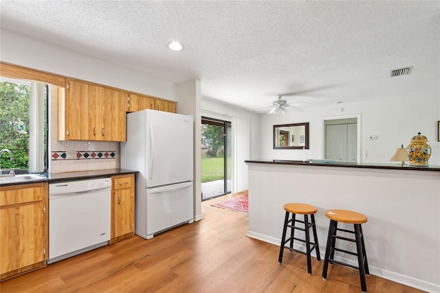 kitchen with white appliances, light wood finished floors, visible vents, dark countertops, and a sink