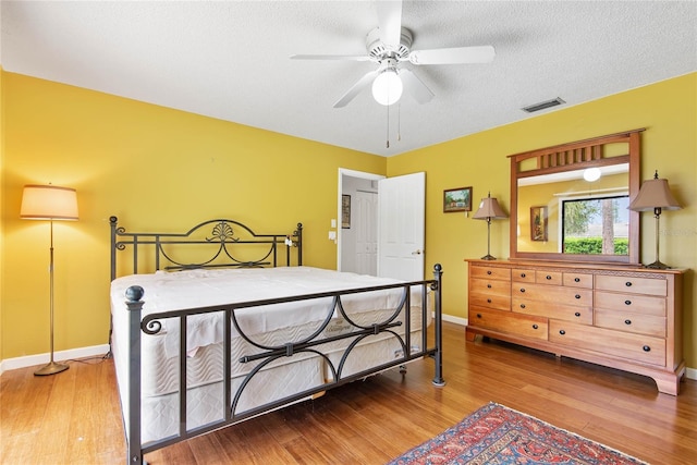 bedroom with a textured ceiling, ceiling fan, wood finished floors, visible vents, and baseboards