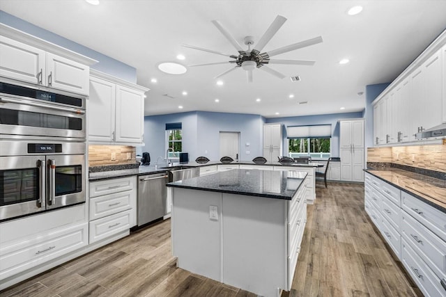 kitchen featuring white cabinetry, stainless steel appliances, decorative backsplash, kitchen peninsula, and dark stone counters