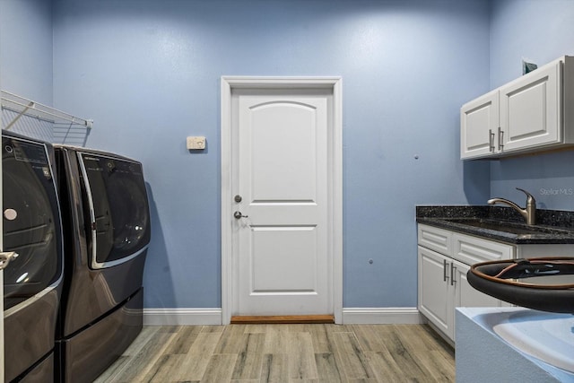 clothes washing area with sink, cabinets, washing machine and dryer, and light hardwood / wood-style floors