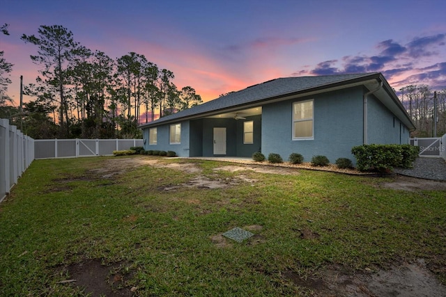 back house at dusk featuring a lawn