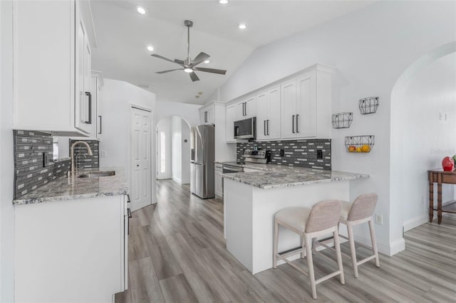 kitchen with sink, light stone counters, kitchen peninsula, stainless steel appliances, and white cabinets