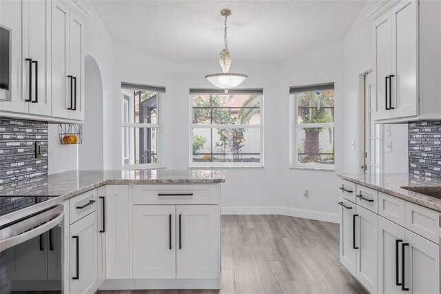 kitchen featuring pendant lighting, tasteful backsplash, white cabinets, light stone counters, and light wood-type flooring