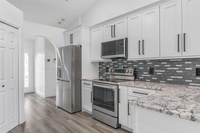 kitchen with appliances with stainless steel finishes, white cabinetry, light stone counters, decorative backsplash, and vaulted ceiling