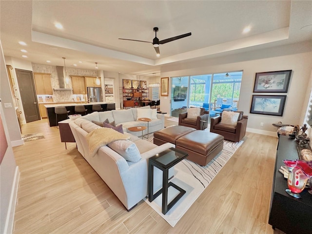 living room with light hardwood / wood-style flooring, ceiling fan, and a tray ceiling