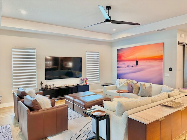 living room with ceiling fan, a tray ceiling, and light hardwood / wood-style flooring