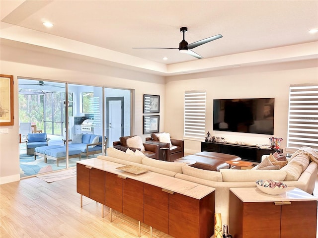 living room featuring ceiling fan, a tray ceiling, and light hardwood / wood-style floors