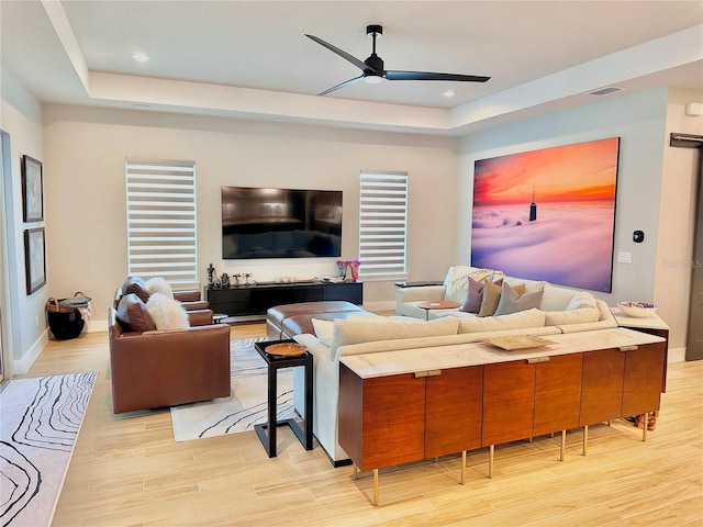 living room featuring light hardwood / wood-style floors, a raised ceiling, and ceiling fan