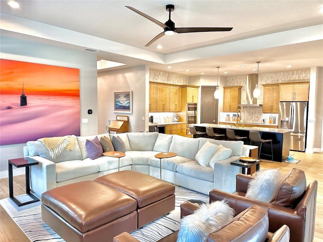 living room featuring ceiling fan, sink, and light hardwood / wood-style floors