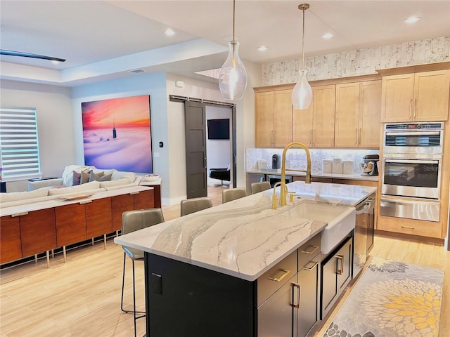 kitchen featuring light stone countertops, a barn door, a center island with sink, and light brown cabinets