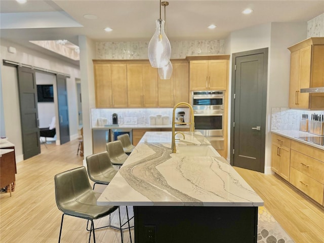 kitchen featuring light brown cabinetry, double oven, decorative backsplash, and a large island with sink