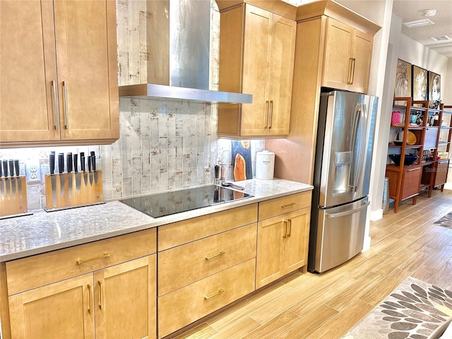 kitchen featuring stainless steel fridge, backsplash, black electric stovetop, light hardwood / wood-style floors, and wall chimney exhaust hood