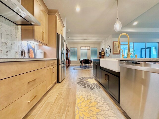 kitchen featuring stainless steel appliances, wall chimney range hood, pendant lighting, and light brown cabinetry