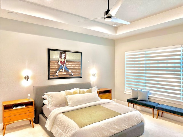 carpeted bedroom with a raised ceiling and ceiling fan