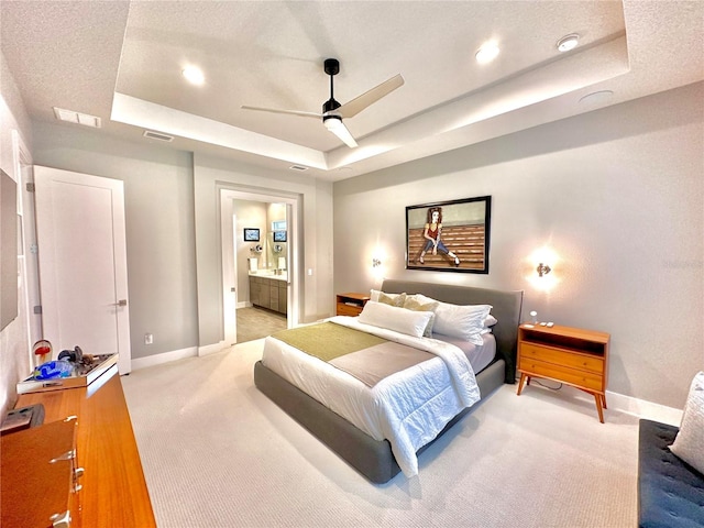 bedroom with a tray ceiling, light colored carpet, ceiling fan, and ensuite bathroom