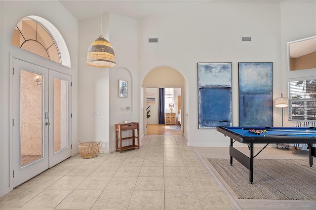 game room with french doors, a towering ceiling, and light tile patterned flooring