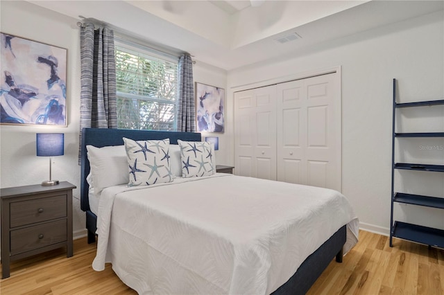 bedroom with ceiling fan, a raised ceiling, a closet, and light wood-type flooring