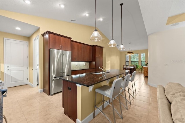 kitchen with sink, a breakfast bar area, high end refrigerator, decorative light fixtures, and a kitchen island with sink