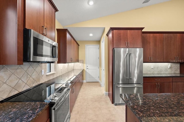 kitchen with lofted ceiling, tasteful backsplash, dark stone counters, and appliances with stainless steel finishes