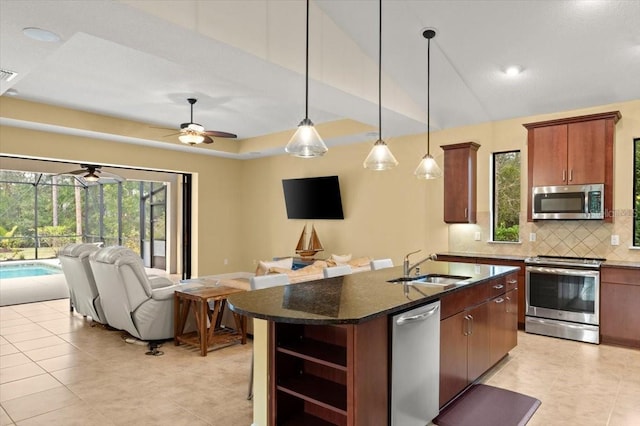 kitchen featuring pendant lighting, an island with sink, sink, decorative backsplash, and stainless steel appliances