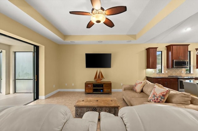 tiled living room with a tray ceiling and ceiling fan