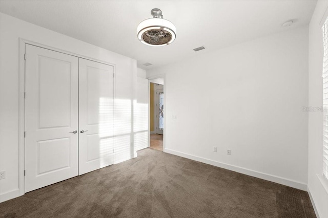 unfurnished bedroom with dark carpet and a closet