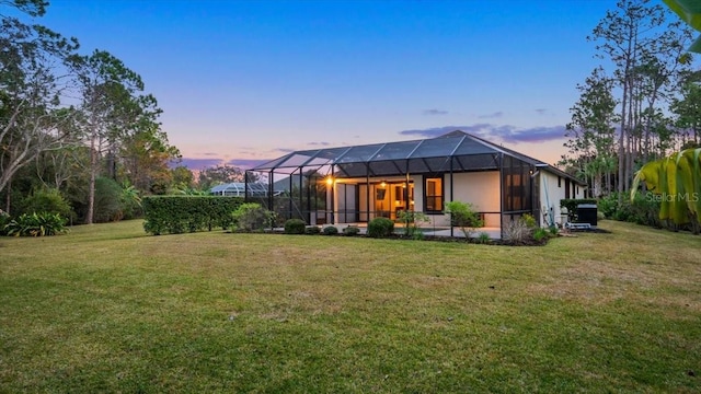 back house at dusk with a lanai and a lawn