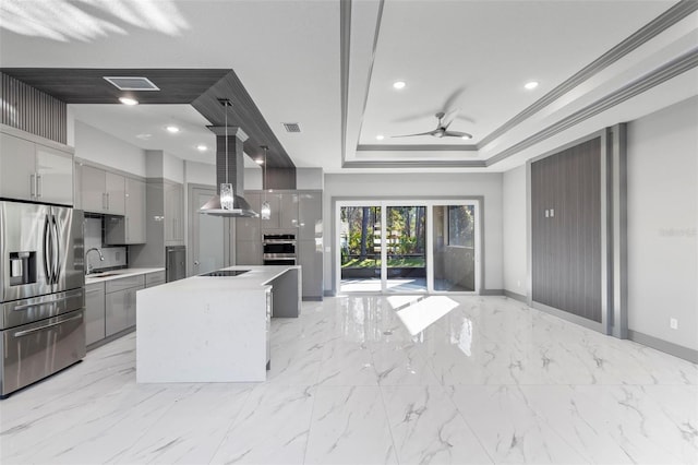 kitchen with pendant lighting, sink, appliances with stainless steel finishes, a tray ceiling, and a kitchen island