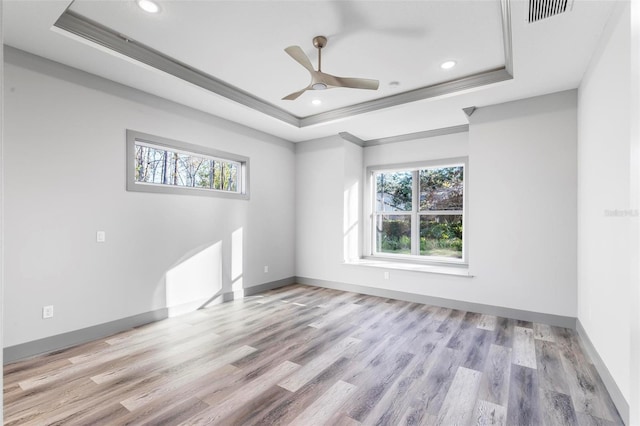 spare room featuring crown molding, a tray ceiling, and light wood-type flooring