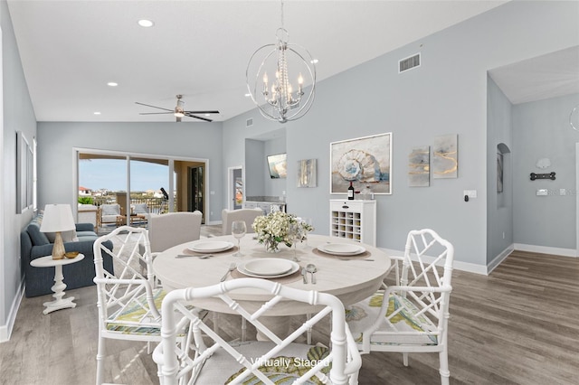 dining space with ceiling fan with notable chandelier, wood-type flooring, and vaulted ceiling