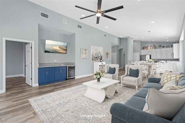 living room with hardwood / wood-style flooring, bar area, beverage cooler, and ceiling fan with notable chandelier