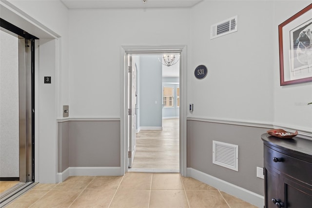 hallway with light tile patterned floors, a notable chandelier, and elevator