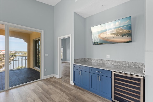 bar featuring wine cooler, light stone counters, blue cabinets, and light wood-type flooring