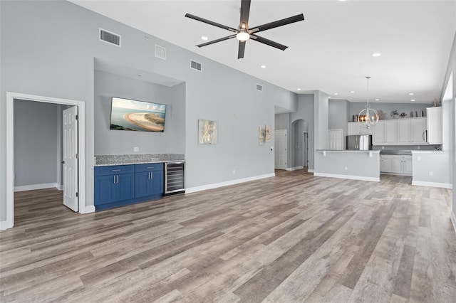 unfurnished living room with ceiling fan with notable chandelier, light hardwood / wood-style flooring, and beverage cooler