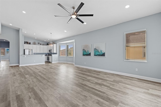 unfurnished living room featuring vaulted ceiling, ceiling fan with notable chandelier, and light wood-type flooring