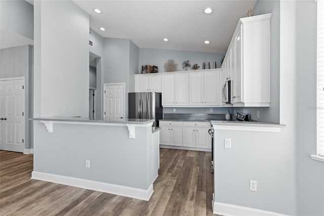 kitchen with hardwood / wood-style flooring, appliances with stainless steel finishes, a kitchen breakfast bar, white cabinets, and vaulted ceiling