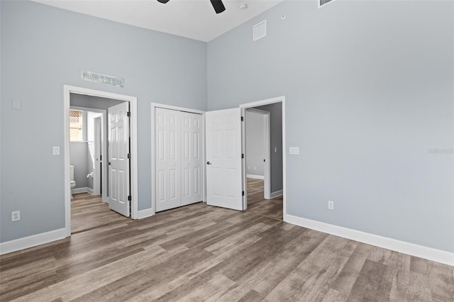 unfurnished bedroom with ceiling fan, ensuite bath, a high ceiling, and light wood-type flooring