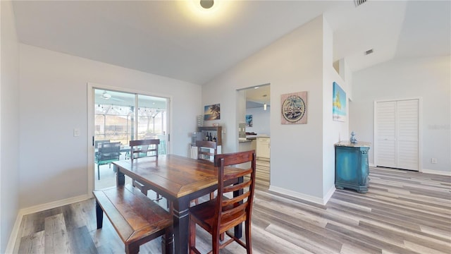 dining area with high vaulted ceiling and light hardwood / wood-style floors